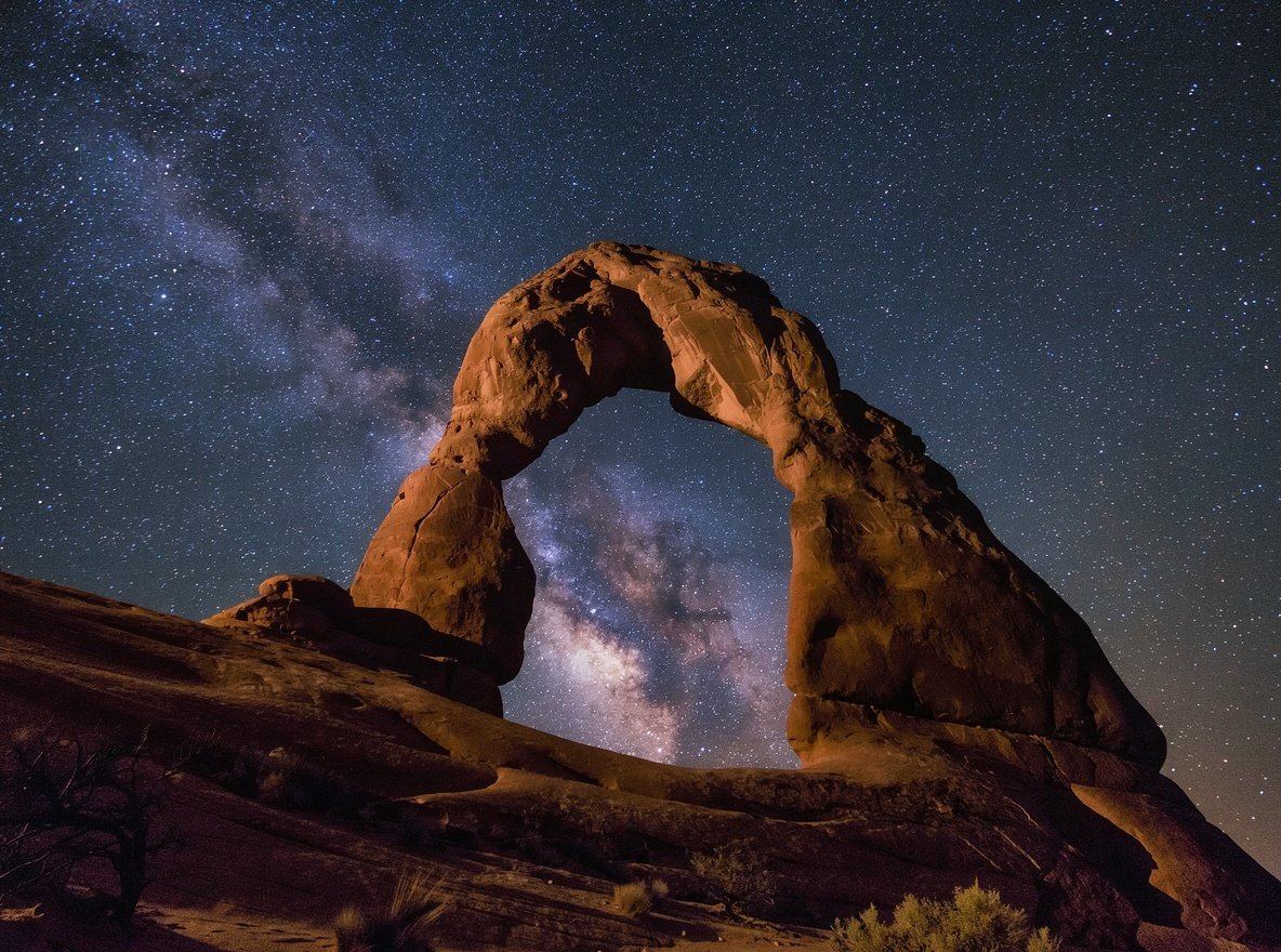 The Milky Way rising over a sandstone arch in Arches National Park at night